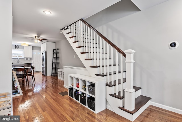 staircase with hardwood / wood-style flooring, a ceiling fan, and baseboards