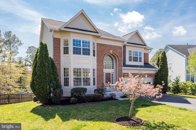 traditional-style home featuring brick siding, driveway, a front lawn, and fence