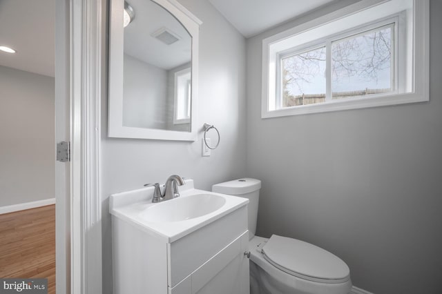 half bath featuring toilet, wood finished floors, vanity, visible vents, and baseboards