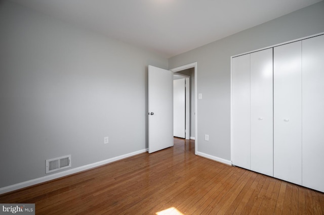 unfurnished bedroom featuring hardwood / wood-style floors, a closet, visible vents, and baseboards