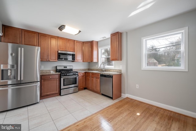 kitchen featuring light tile patterned floors, baseboards, brown cabinetry, appliances with stainless steel finishes, and a sink