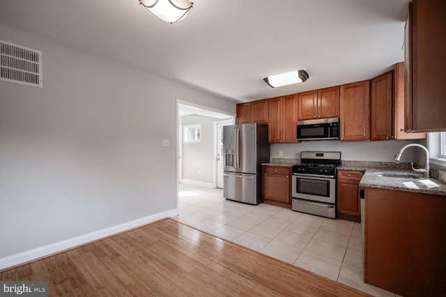 kitchen with light wood finished floors, visible vents, brown cabinetry, stainless steel appliances, and a sink