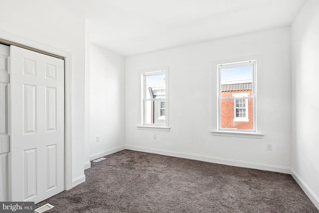 unfurnished bedroom featuring dark carpet, visible vents, and baseboards