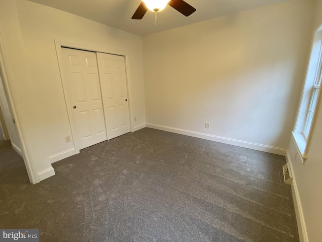 unfurnished bedroom with baseboards, dark carpet, and a closet