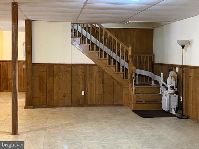 stairs featuring a wainscoted wall, a paneled ceiling, and wooden walls