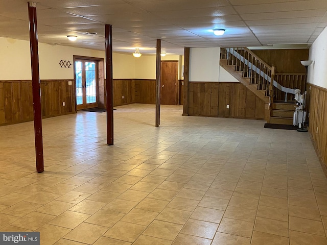 below grade area featuring a wainscoted wall, wooden walls, stairs, and a drop ceiling