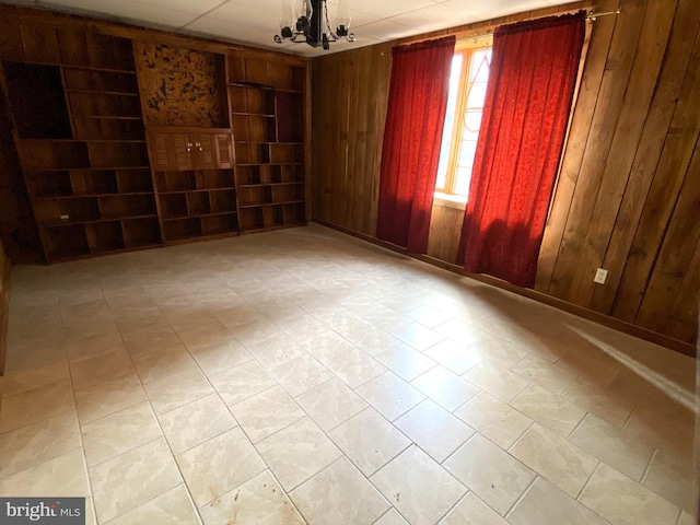 spare room featuring a chandelier, wooden walls, and built in shelves