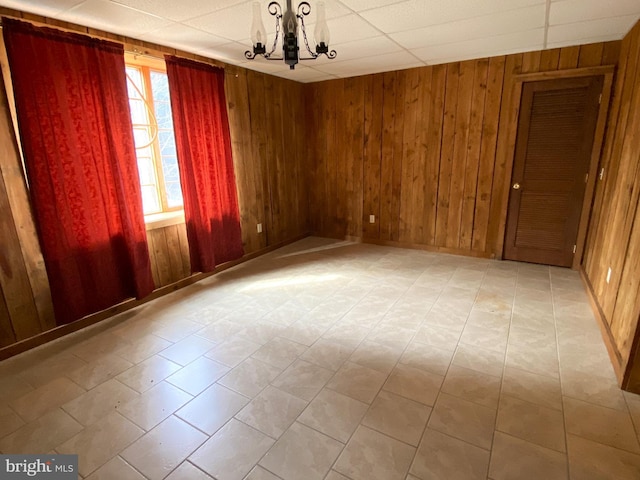 unfurnished room with a paneled ceiling, wood walls, and an inviting chandelier