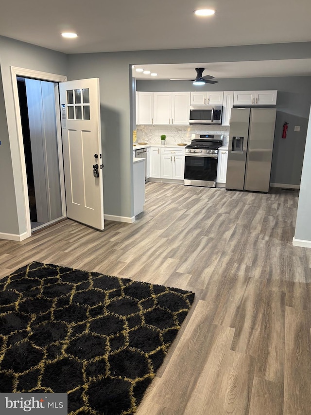 kitchen featuring stainless steel appliances, decorative backsplash, white cabinets, and light wood-style floors