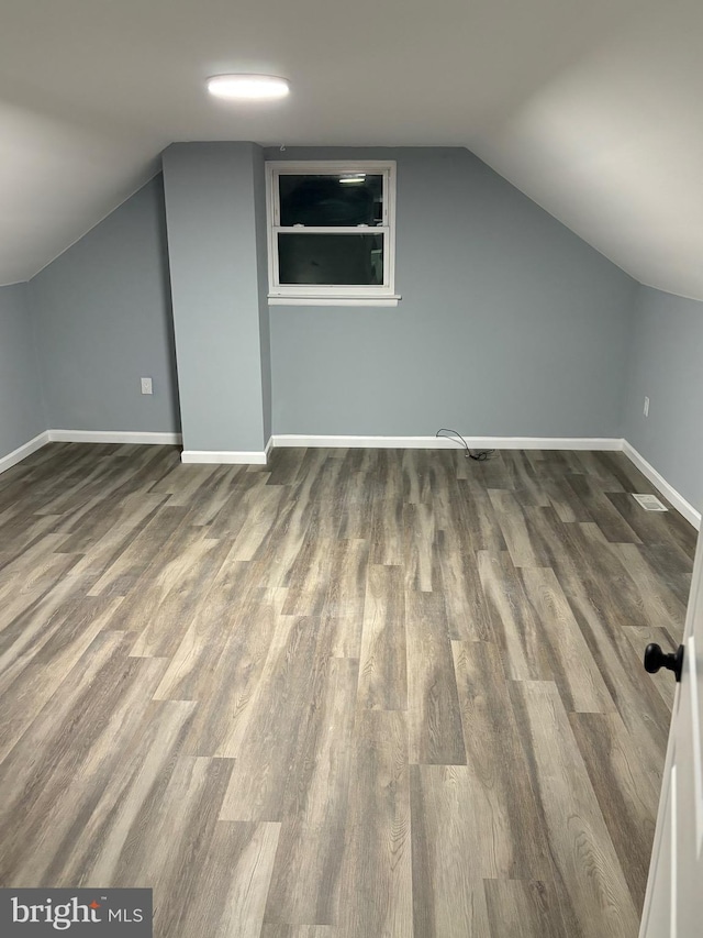 bonus room with baseboards, vaulted ceiling, and dark wood-style flooring