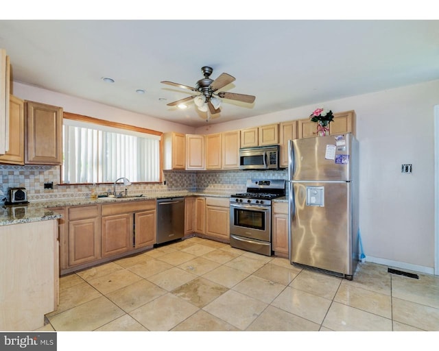 kitchen featuring light stone counters, a sink, a ceiling fan, appliances with stainless steel finishes, and backsplash