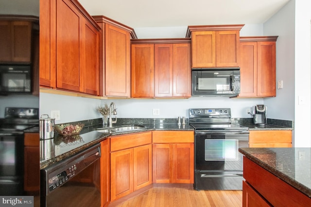 kitchen with brown cabinets, light wood-style flooring, a sink, dark stone countertops, and black appliances