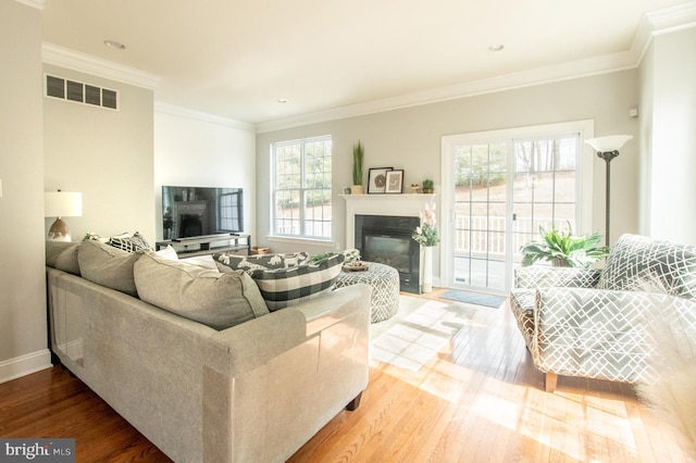 living area with a fireplace with flush hearth, wood finished floors, baseboards, visible vents, and crown molding