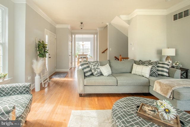 living area with baseboards, light wood-type flooring, visible vents, and crown molding