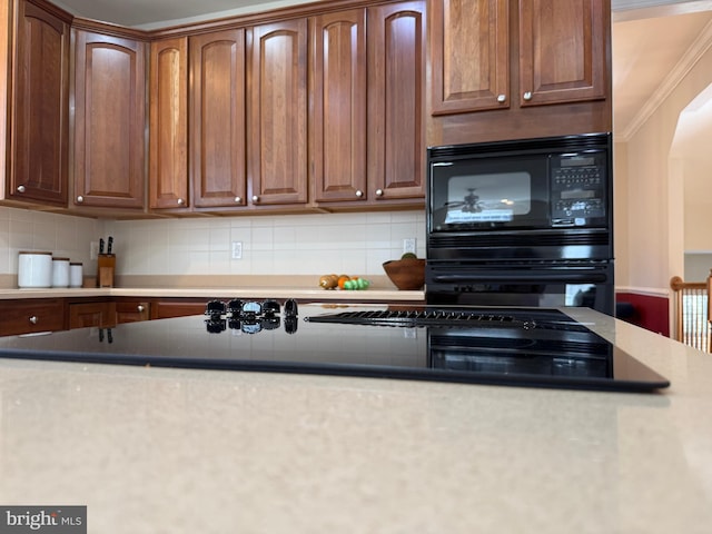 kitchen with arched walkways, black appliances, ornamental molding, and backsplash