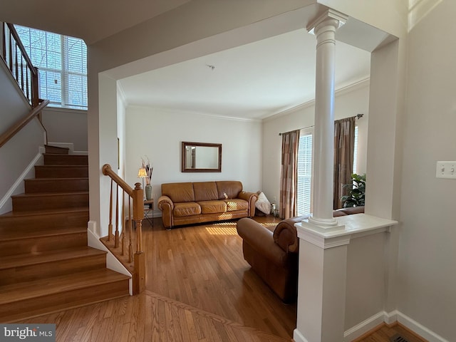 living room with wood finished floors, baseboards, ornamental molding, stairway, and ornate columns