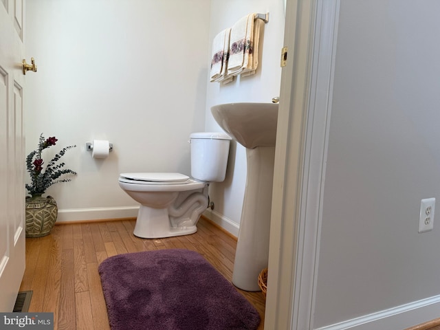 half bath featuring baseboards, visible vents, toilet, and wood finished floors