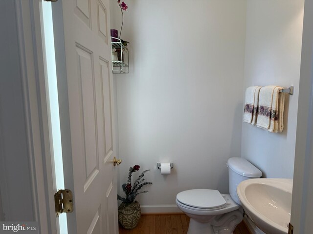 half bath featuring toilet, baseboards, a sink, and wood finished floors