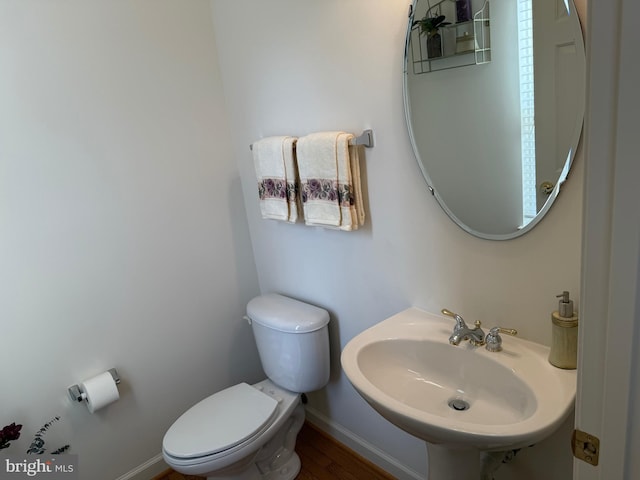 half bath with baseboards, a sink, and toilet