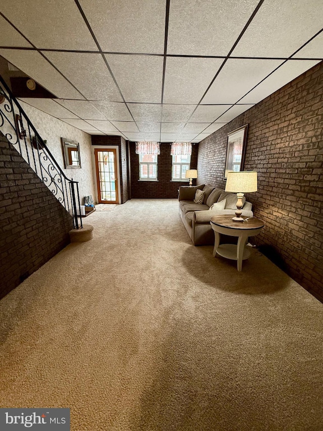 unfurnished room featuring carpet, a drop ceiling, brick wall, and stairs