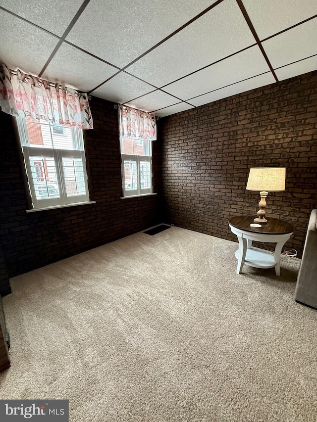 interior space with a paneled ceiling, brick wall, and carpet