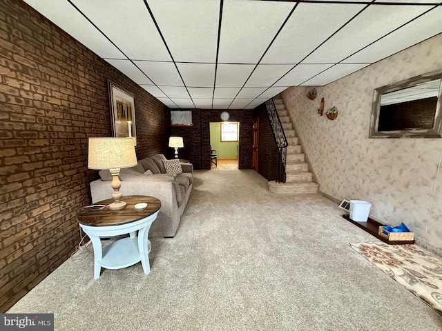 unfurnished living room featuring brick wall, a drop ceiling, stairway, and carpet