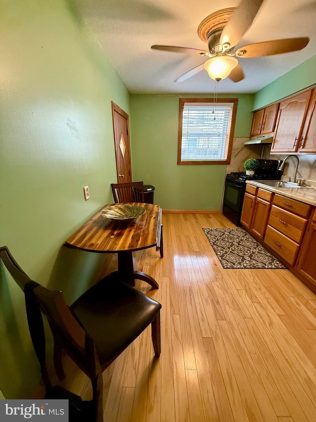 kitchen with black range with gas cooktop, light wood-style floors, brown cabinets, light countertops, and under cabinet range hood