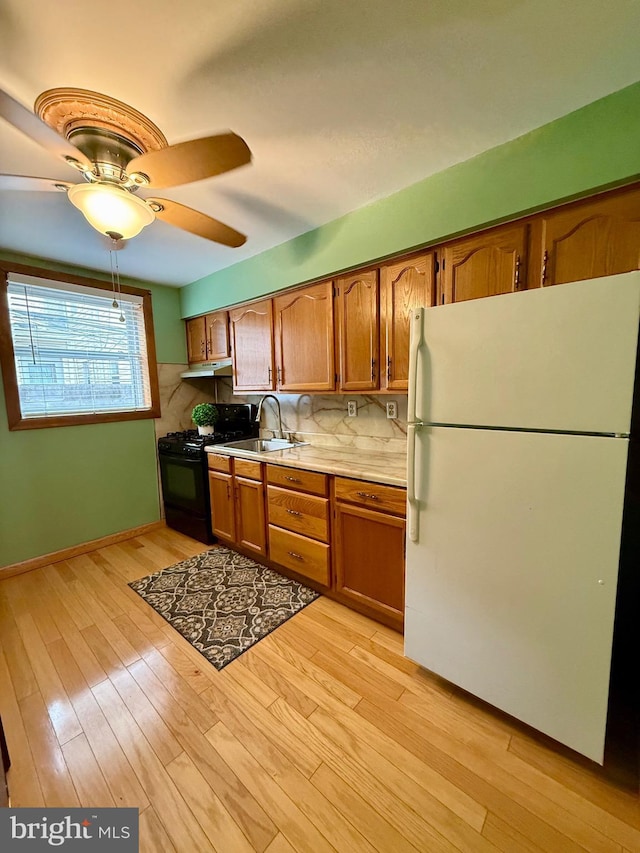 kitchen with light countertops, light wood-style floors, freestanding refrigerator, black gas stove, and a sink