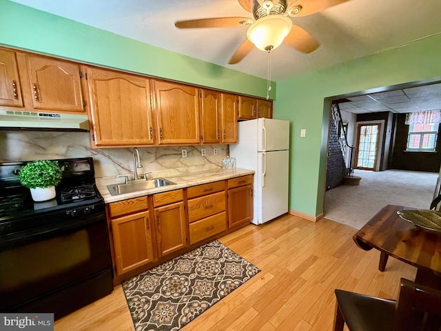 kitchen with under cabinet range hood, a sink, black gas stove, light countertops, and freestanding refrigerator