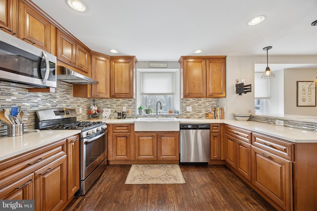 kitchen featuring brown cabinets, appliances with stainless steel finishes, a sink, a peninsula, and under cabinet range hood