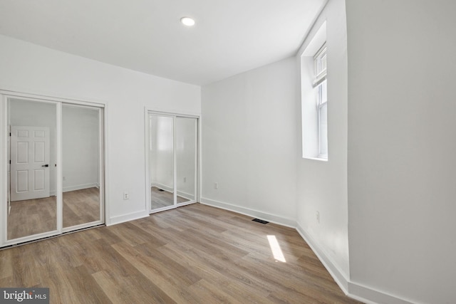 unfurnished bedroom featuring multiple closets, recessed lighting, visible vents, wood finished floors, and baseboards