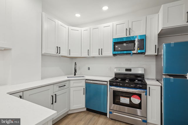 kitchen featuring stainless steel appliances, light countertops, white cabinets, a sink, and light wood-type flooring