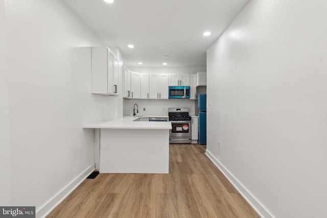 kitchen with light wood finished floors, stainless steel appliances, light countertops, white cabinetry, and a peninsula