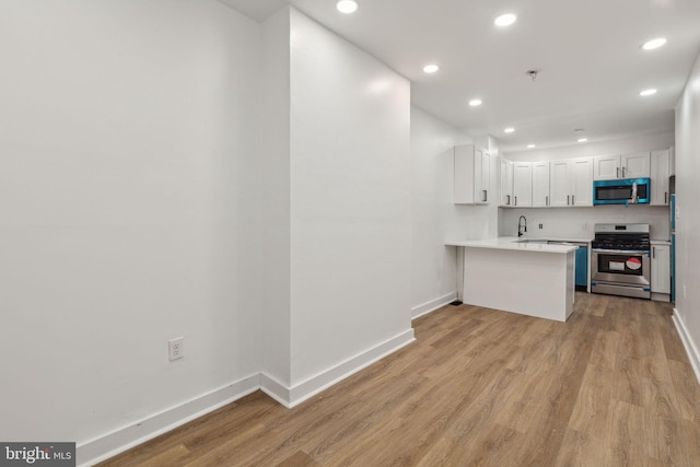 kitchen with baseboards, appliances with stainless steel finishes, light countertops, light wood-type flooring, and a sink