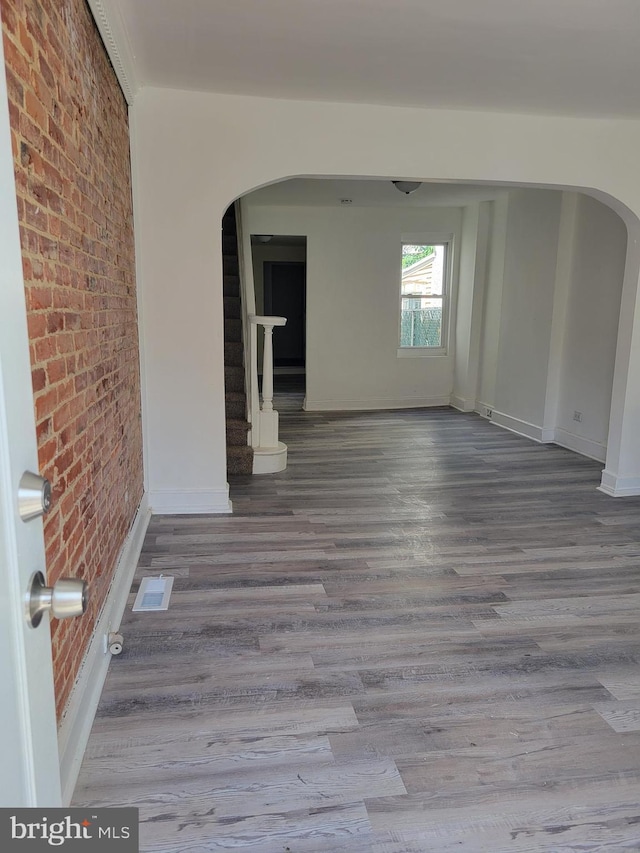 unfurnished room with brick wall, stairs, arched walkways, and wood finished floors