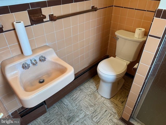 bathroom with tile walls, toilet, a stall shower, and a sink