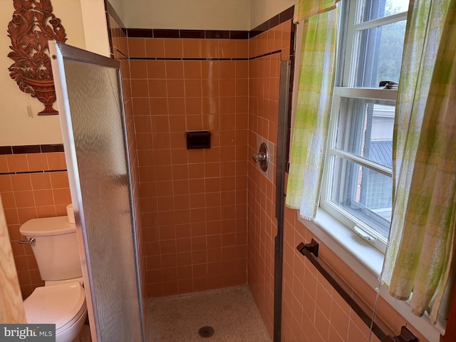 bathroom with a wealth of natural light, toilet, a stall shower, and tile walls