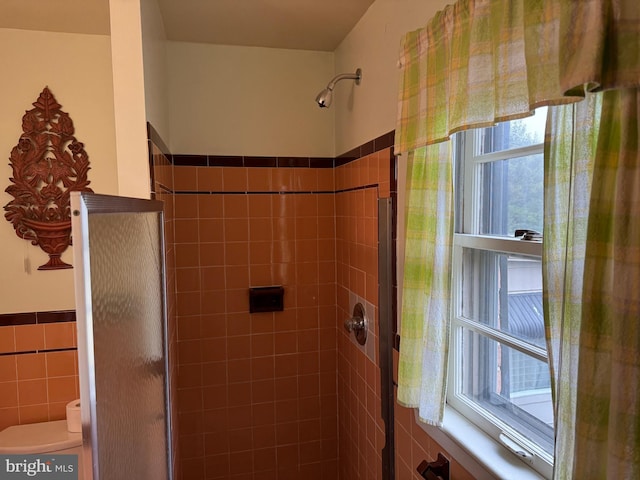 bathroom featuring a shower stall, toilet, tile walls, and wainscoting