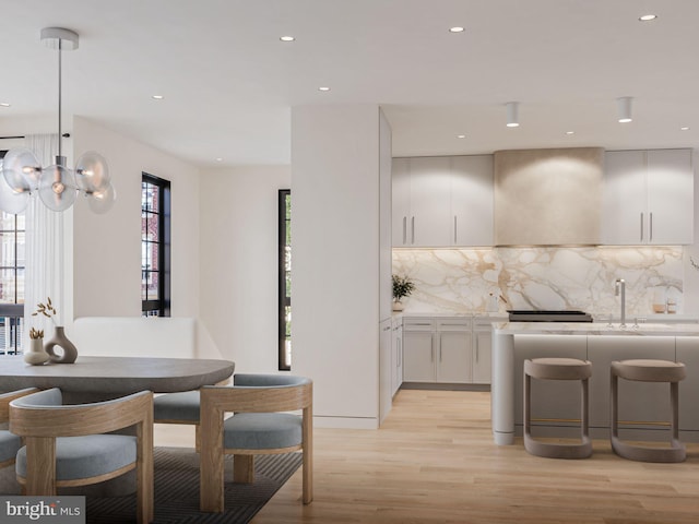 kitchen featuring decorative backsplash, light countertops, light wood-type flooring, wall chimney range hood, and white cabinetry