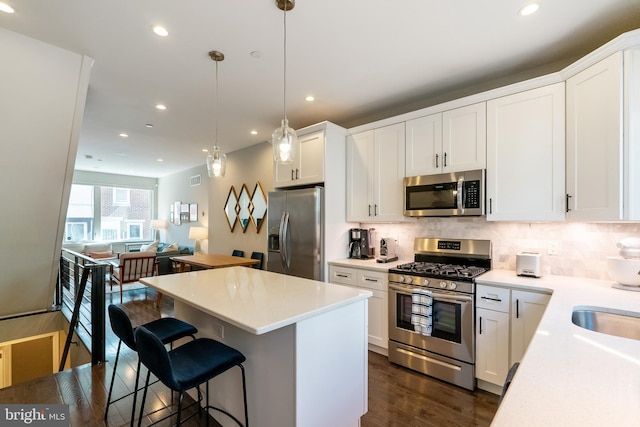 kitchen with a kitchen island, dark wood finished floors, stainless steel appliances, a kitchen bar, and tasteful backsplash