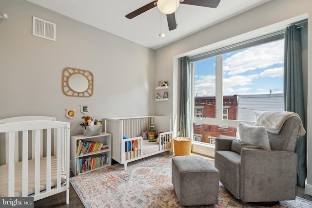 bedroom with visible vents, a nursery area, and wood finished floors