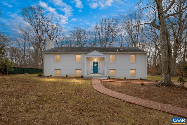 split foyer home featuring a chimney, a front yard, and fence