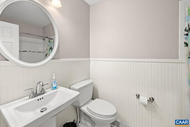 bathroom featuring toilet, a shower with shower curtain, a sink, and wainscoting