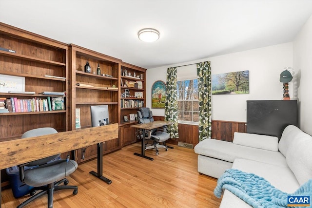 home office featuring light wood-style flooring, visible vents, and wainscoting