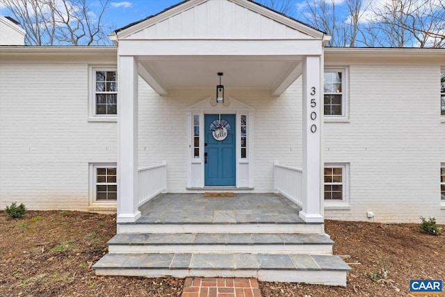 doorway to property featuring board and batten siding, covered porch, and brick siding