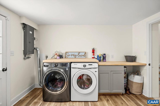 washroom featuring light wood-style flooring, baseboards, cabinet space, electric panel, and washer and clothes dryer