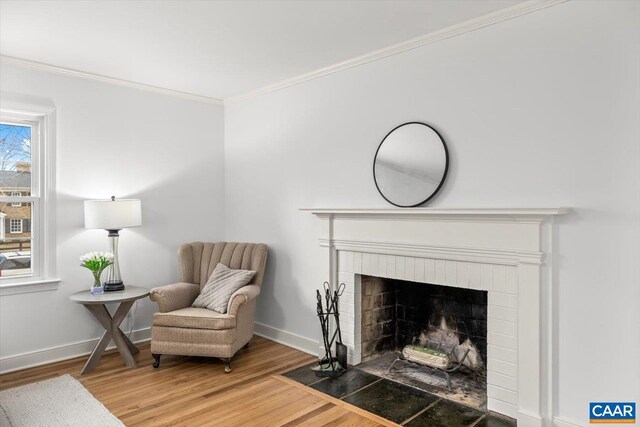 sitting room with a brick fireplace, baseboards, ornamental molding, and wood finished floors