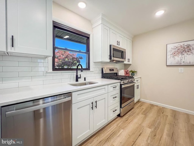 kitchen with stainless steel appliances, decorative backsplash, white cabinets, a sink, and light wood-type flooring