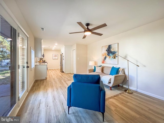 living area featuring baseboards, ceiling fan, visible vents, and light wood finished floors