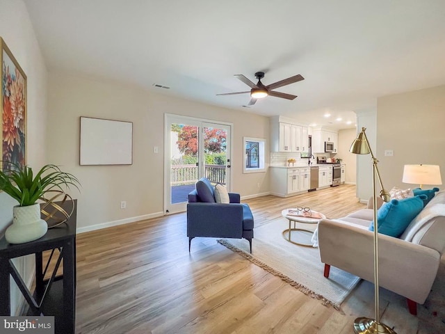 living room featuring light wood-style floors, visible vents, baseboards, and a ceiling fan